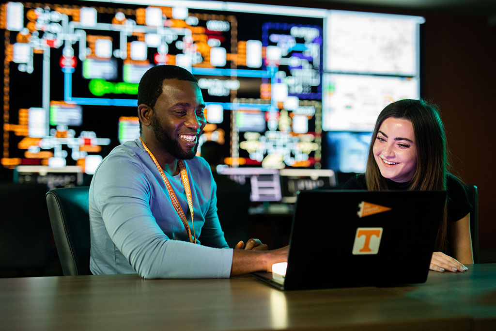 A Black man uses a laptop while a woman watches in CURENT's Visualization Lab.